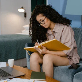 Woman reading a book sitting on the couch with a laptop in front of her